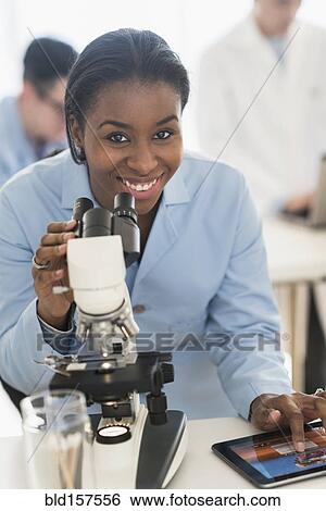 Stock Photograph - Scientist using microscope and digital tablet in research laboratory. Fotosearch