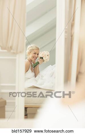 Stock Photo - Smiling bride admiring herself in mirror on bed. Fotosearch