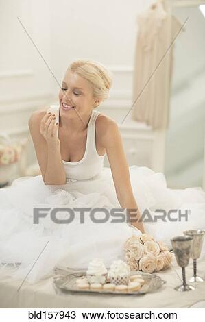 Stock Image - Smiling bride eating cupcakes on bed. Fotosearch