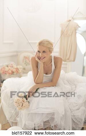Stock Image - Smiling bride sitting with bouquet on bed. Fotosearch