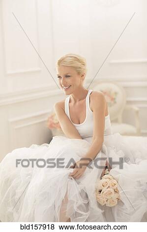 Stock Photo - Smiling bride sitting with bouquet on bed. Fotosearch