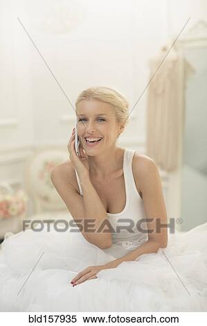 Stock Photography - Smiling bride talking on cell phone on bed. Fotosearch