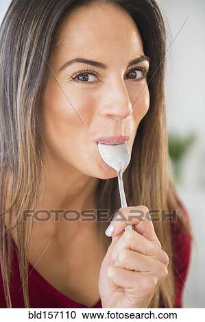 Stock Image - Smiling Caucasian woman licking spoon. Fotosearch