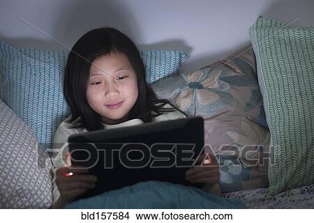 Picture - Smiling Chinese girl watching digital tablet in bed. Fotosearch