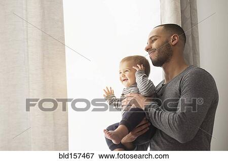 Stock Photo - Smiling father and baby son looking out window. Fotosearch