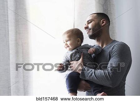 Stock Photo - Smiling father and baby son looking out window. Fotosearch