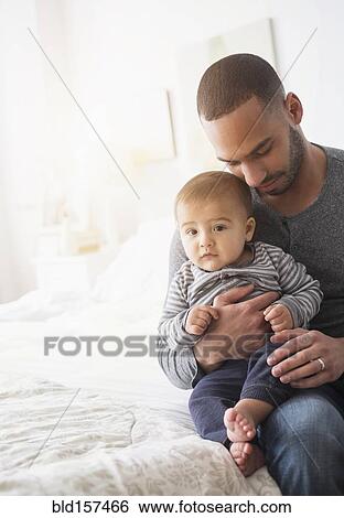 Smiling father holding baby son on bed View Large Photo Image Stock Photograph - Smiling father holding baby son on bed. Fotosearch