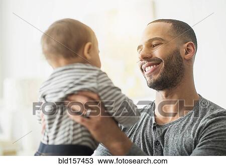Stock Image - Smiling father holding baby son. Fotosearch