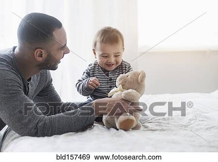 Smiling father playing with baby son on bed View Large Photo Image Stock Photo - Smiling father playing with baby son on bed. Fotosearch