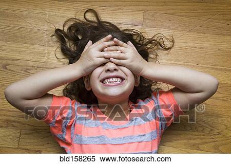 Stock Photography - Smiling Hispanic girl covering her eyes on floor. Fotosearch