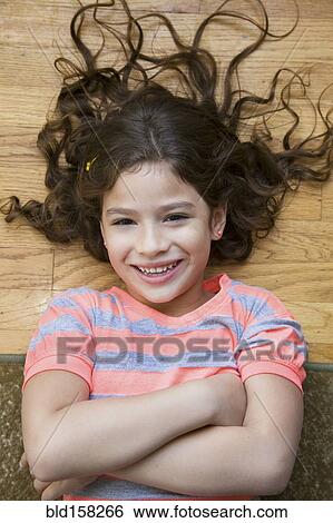 Stock Photograph - Smiling Hispanic girl laughing on floor. Fotosearch