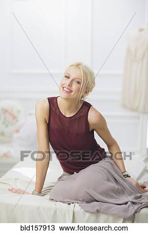 Stock Image - Smiling woman sitting on bed. Fotosearch