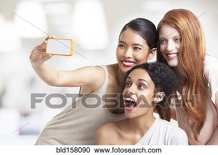 Stock Image - Smiling women taking cell phone selfie. Fotosearch