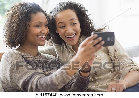Stock Image - Smiling women taking cell phone photograph. Fotosearch
