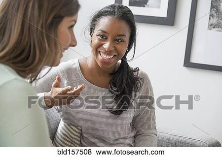Stock Photo - Smiling women talking on sofa. Fotosearch