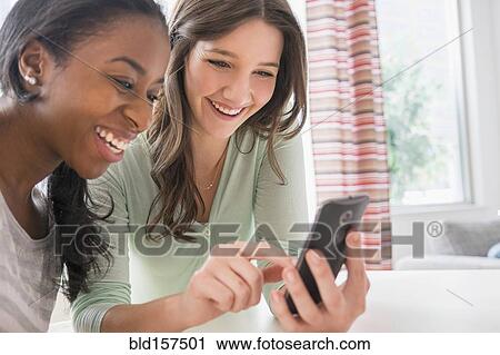 Stock Image - Smiling women texting on cell phone. Fotosearch