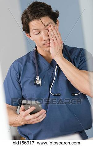 Stock Photo - Tired Hispanic doctor holding cell phone in hospital. Fotosearch