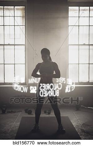 Stock Image - Virtual words circling Black athlete checking fitness tracker. Fotosearch