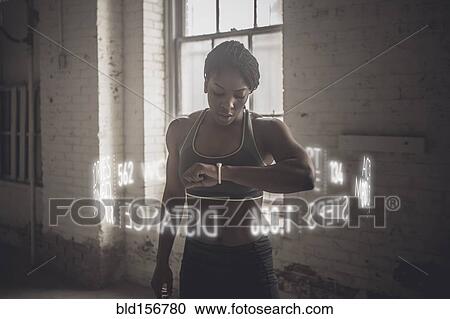Stock Image - Virtual words circling Black athlete checking fitness tracker. Fotosearch