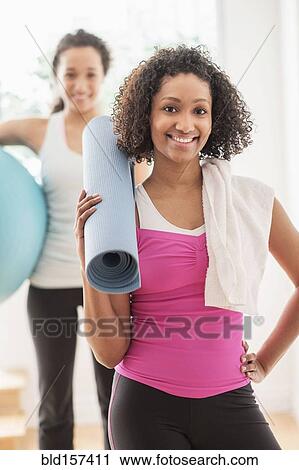 Stock Image - Woman carrying yoga mat in exercise class. Fotosearch