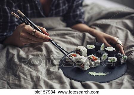 Woman eating sushi with chopsticks in bed View Large Photo Image Picture - Woman eating sushi with chopsticks in bed. Fotosearch
