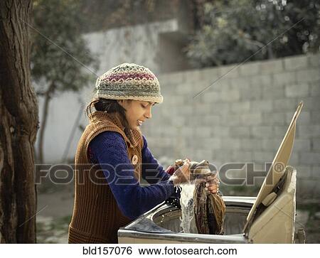 Stock Photograph - Woman in knit hat hand-washing clothing outdoors. Fotosearch