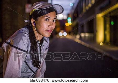 Stock Photograph - Asian runner resting on city street at night. Fotosearch