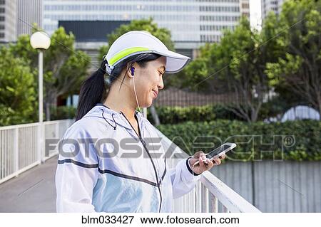 Stock Photo - Asian runner using cell phone in city. Fotosearch