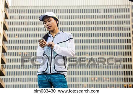 Stock Image - Asian runner using cell phone near highrise building. Fotosearch