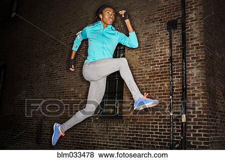 Black woman leaping near brick wall at night View Large Photo Image Stock Photo - Black woman leaping near brick wall at night. Fotosearch