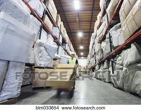 Picture - Blurred view of Caucasian worker wheeling cardboard box in warehouse. Fotosearch