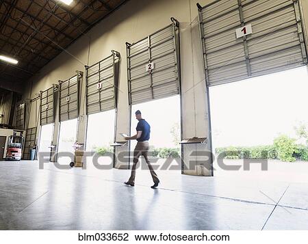 Stock Image - Blurred view of Caucasian worker walking in warehouse. Fotosearch