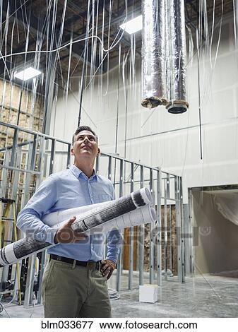 Stock Photo - Caucasian architect carrying blueprints at construction site. Fotosearch