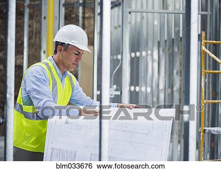 Stock Photograph - Caucasian architect reading blueprints at construction site. Fotosearch