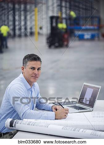 Stock Image - Caucasian architect working in warehouse. Fotosearch
