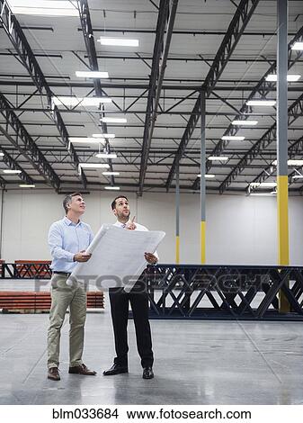 Picture - Caucasian architects reading blueprints in warehouse. Fotosearch