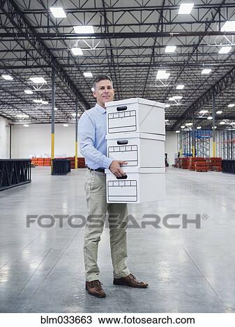 Stock Image - Caucasian businessman carrying boxes in empty warehouse. Fotosearch