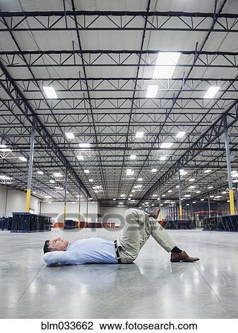 Stock Image - Caucasian businessman laying on floor in empty warehouse. Fotosearch