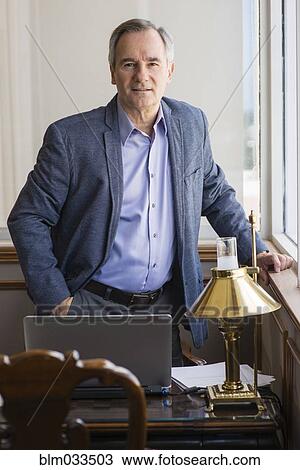 Stock Image - Caucasian businessman standing at office desk. Fotosearch