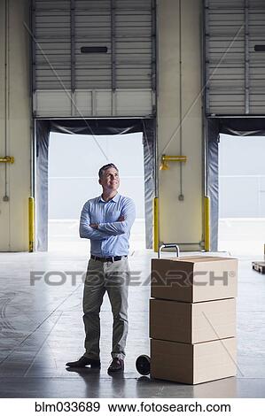 Caucasian businessman standing near cardboard boxes in warehouse View Large Photo Image Stock Photo - Caucasian businessman standing near cardboard boxes in warehouse. Fotosearch