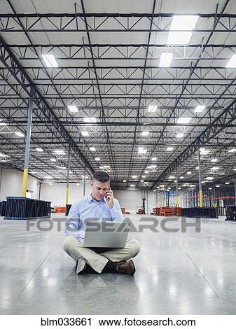 Stock Image - Caucasian businessman using laptop in empty warehouse. Fotosearch
