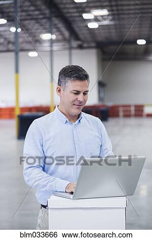 Stock Photograph - Caucasian businessman using laptop in empty warehouse. Fotosearch