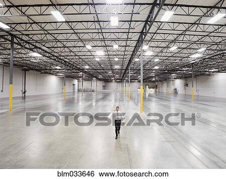 Stock Photograph - Caucasian businessman walking in empty warehouse. Fotosearch