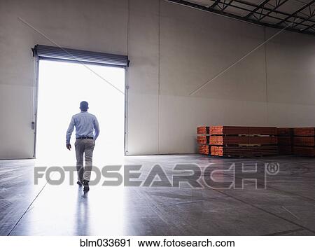 Stock Image - Caucasian businessman walking in warehouse. Fotosearch