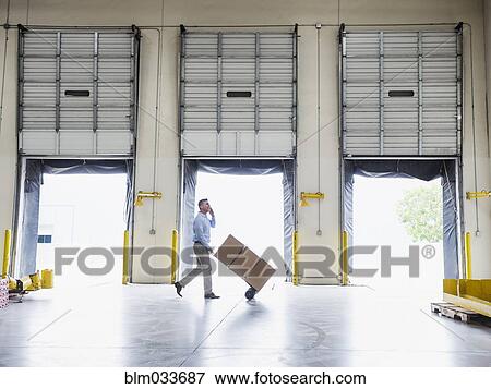 Caucasian businessman wheeling cardboard boxes in warehouse View Large Photo Image Stock Photo - Caucasian businessman wheeling cardboard boxes in warehouse. Fotosearch