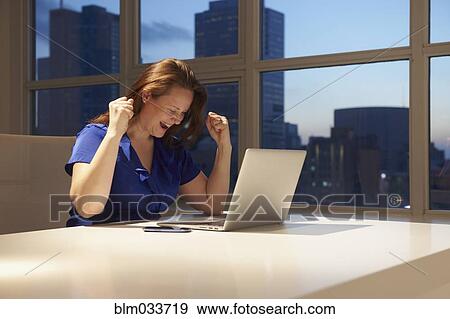 Stock Photo - Caucasian businesswoman cheering at laptop in office. Fotosearch