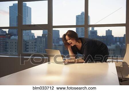 Stock Image - Caucasian businesswoman laughing at laptop in office. Fotosearch