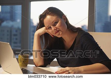 Stock Image - Caucasian businesswoman smiling at laptop in office. Fotosearch
