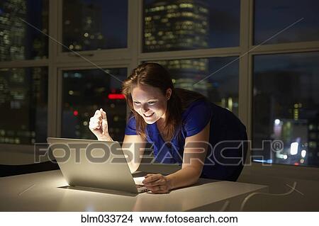 Picture - Caucasian businesswoman working on laptop in office at night. Fotosearch