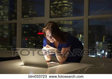 Stock Image - Caucasian businesswoman working on laptop in office at night. Fotosearch
